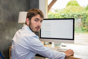 portrait d'un jeune homme employé en train de travailler assis devant son ordinateur, ou bien en...