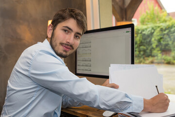 jeune homme au travail ou en télétravail devant un ordinateur en train d'écrire et regardant...
