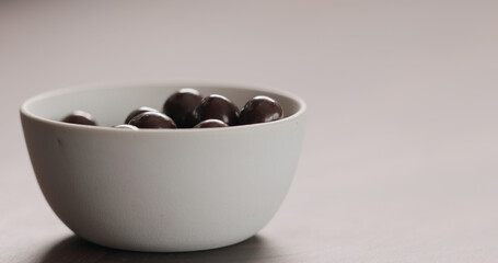 chocolate covered hazelnuts in white bowl on walnut table