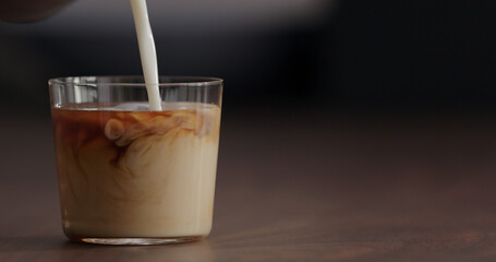 pour milk into ice coffee on black walnut table