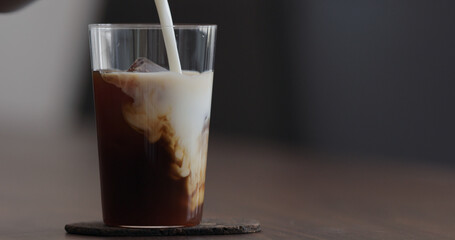 pour milk into ice coffee on black walnut table