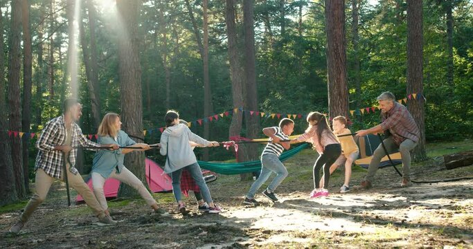 Full length view of the kids at summer camp playing tug or war with their senior teacher at the forest. Happy childhood and activities concept