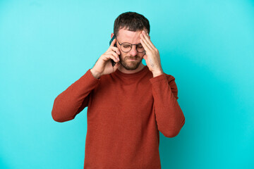 Young Brazilian man using mobile phone isolated on blue background with tired and sick expression