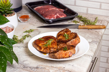Fresh prepared roasted beef steak with spices and rosemary on white round plate on the kitchen table background.