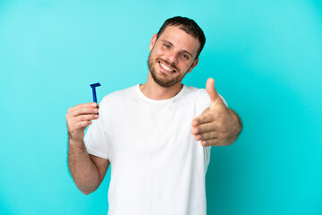 Brazilian man shaving his beard isolated on blue background shaking hands for closing a good deal