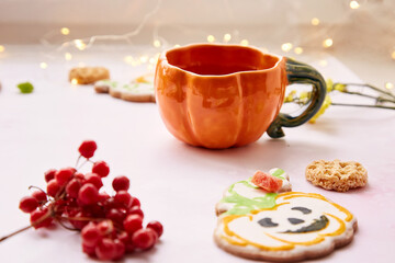 Halloween creative concept: pumpkin cup and sweet cookies in shape of festive pumpkins. Atmospheric aesthetic autumn mood or trick or treat concept. Viburnum and candied fruit decorations