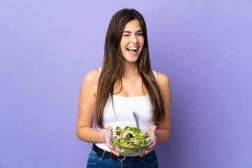 Teenager Brazilian girl holding a salad over isolated purple background