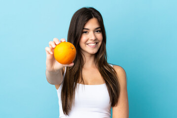 Teenager Brazilian girl over isolated blue background holding an orange