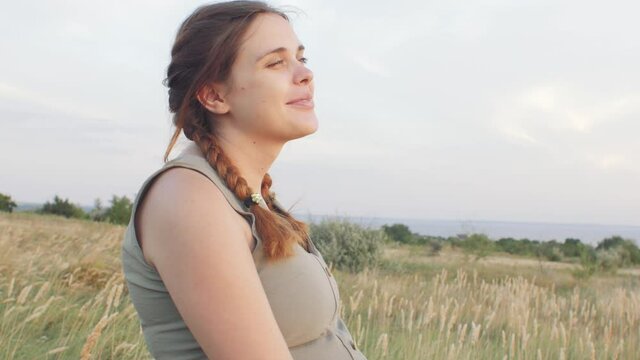 young happy beautiful pregnant woman walks in field among dry fluffy grass at sunset, relaxation on summer nature, preparation for childbirth, healthy motherhood