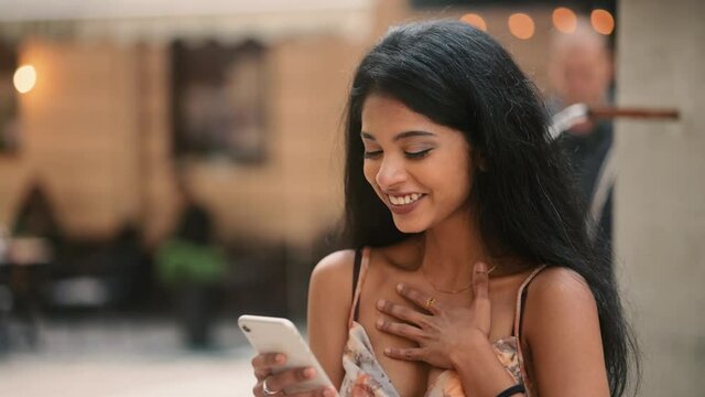 Portrait of happy Indian girl enjoying success on mobile phone at city street. Closeup joyful young woman reading good news on phone in slow motion. . High quality 4k footage