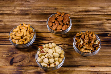 Various nuts (almond, cashew, hazelnut, walnut) in glass bowls on a wooden table. Vegetarian meal. Healthy eating concept