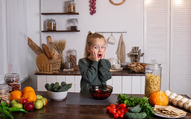a surprised little blonde girl is sitting at a table with fruits and vegetables
