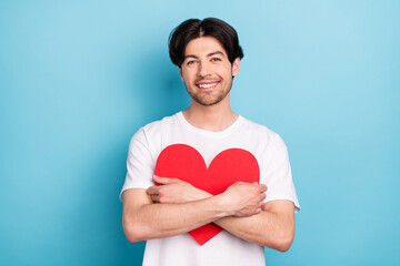 Photo of optimistic millennial brunet guy hug heart wear white t-shirt isolated on blue color background