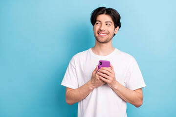 Photo of funny millennial brunet guy hold telephone look empty space wear white t-shirt isolated on blue color background