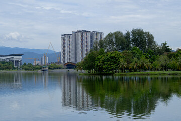 peaceful scene of cityscape in Kepong, Kuala Lumpur, Malaysia. Greenery woods, high-rise buildings, hills and clear cloud sky in background with reflection on water. 