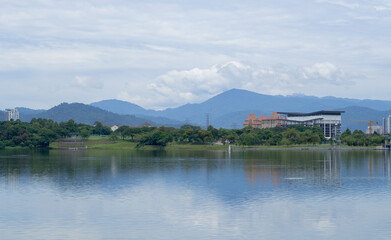 Landscape of Kepong lake in Kuala Lumpur during sunny day with reflection on water, clouds and mountains in the background. 