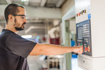 Close-up of machinist pressing emergency stop button on control panel