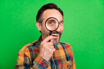Portrait of attractive cheerful amazed man holding looking glass find solution isolated over bright green color background