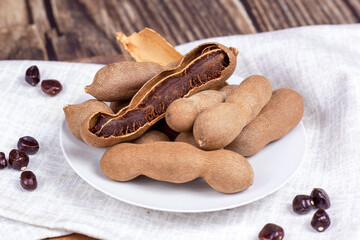 Fresh brown tamarind fruit pods ripe with seeds on light textile background close up.