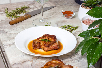 Fresh prepared roasted beef steak with spices and rosemary on white round plate on the kitchen table background.