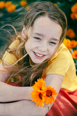 Portrait of pretty girl sitting in field with vibrant gazania wildflowers