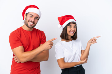 Young couple with christmas hat isolated on white background pointing finger to the side in lateral position