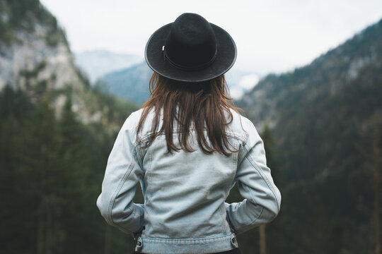 Closeup back view of woman in denim jacket and black hat looking at mountain view, isolated dark background