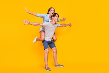 Fototapeta na wymiar Full length body size view of attractive cheerful carefree couple piggy backing flight jet isolated vivid yellow color background