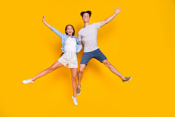 Fototapeta na wymiar Full length body size view of attractive cheery trendy couple jumping having fun good mood isolated vivid yellow color background