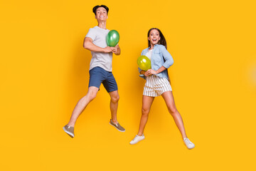 Full length body size view of nice trendy cheerful couple jumping holding balls isolated over bright yellow color background
