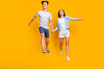 Fototapeta na wymiar Full length body size view of nice cheerful couple jumping running trip isolated over bright yellow color background