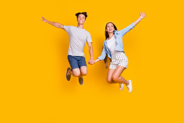 Full length body size view of attractive cheerful couple jumping having fun rest isolated over bright yellow color background