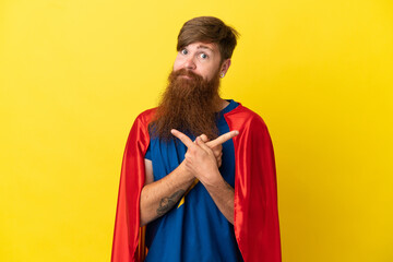Redhead Super Hero man isolated on yellow background pointing to the laterals having doubts