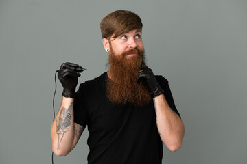 Tattoo artist redhead man isolated on blue background having doubts while looking up