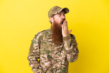 Military Redhead man over isolated on yellow background yawning and covering wide open mouth with hand