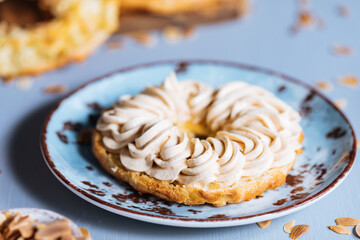 Dessert called Paris Brest on a grey background with powder sugar and almond leaves and almond creme between