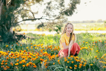 Naklejka na ściany i meble Portrait of pretty girl sitting in field with vibrant gazania wildflowers