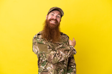 Military Redhead man over isolated on yellow background pointing back