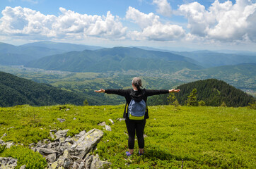 Fototapeta na wymiar Tourist girl hiker with backpack raised arm hands and looking to valley and enjoying this view in Carpathian Mountains, Ukraine
