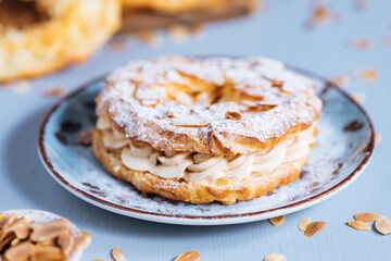 Dessert called Paris Brest on a grey background with powder sugar and almond leaves and almond...