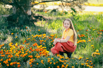 Portrait of pretty girl sitting in field with vibrant gazania wildflowers