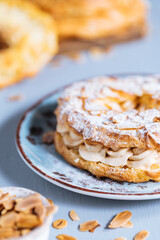 Dessert called Paris Brest on a grey background with powder sugar and almond leaves and almond creme between
