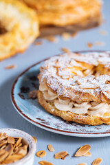 Dessert called Paris Brest on a grey background with powder sugar and almond leaves and almond creme between
