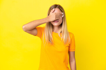 Blonde Uruguayan girl isolated on yellow background covering eyes by hands. Do not want to see...