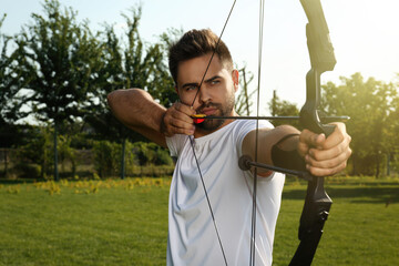 Man with bow and arrow practicing archery in park - obrazy, fototapety, plakaty