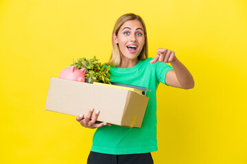 Young Uruguayan girl making a move while picking up a box full of things isolated on yellow...