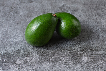 two green avocados lie on an artificial stone board. diet food. green vegetable.