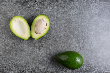 two green avocados lie on an artificial stone board. diet food. green vegetable.avocado cutaway. avocado seed. space for design and for text