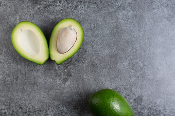 two green avocados lie on an artificial stone board. diet food. green vegetable.avocado cutaway....