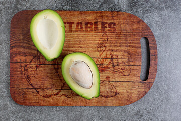 two halves of an avocado. avocado seed. wooden cutting board. artificial stone board. diet food.